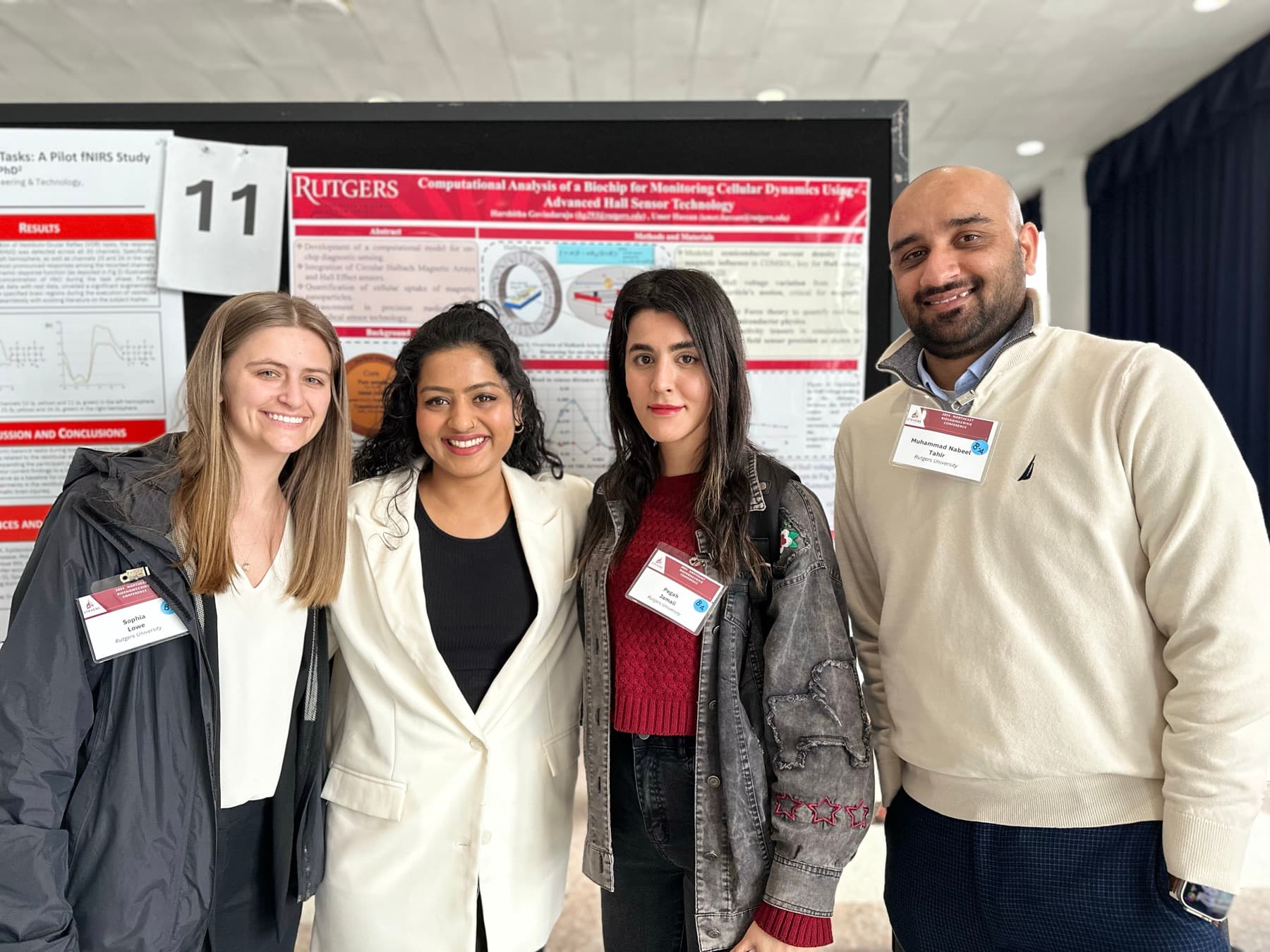 Harshitha with her Hassan Lab research group at the Rutgers Northeast Bioengineering Conference, in front of her Hall-sensor biochip poster.